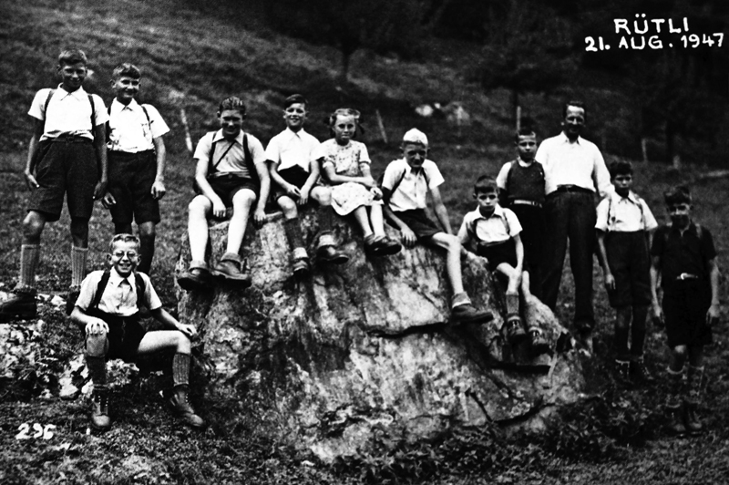 11 Jungs und deren Lehrer posieren mit einem grossen Stein auf der Rütliswiese.