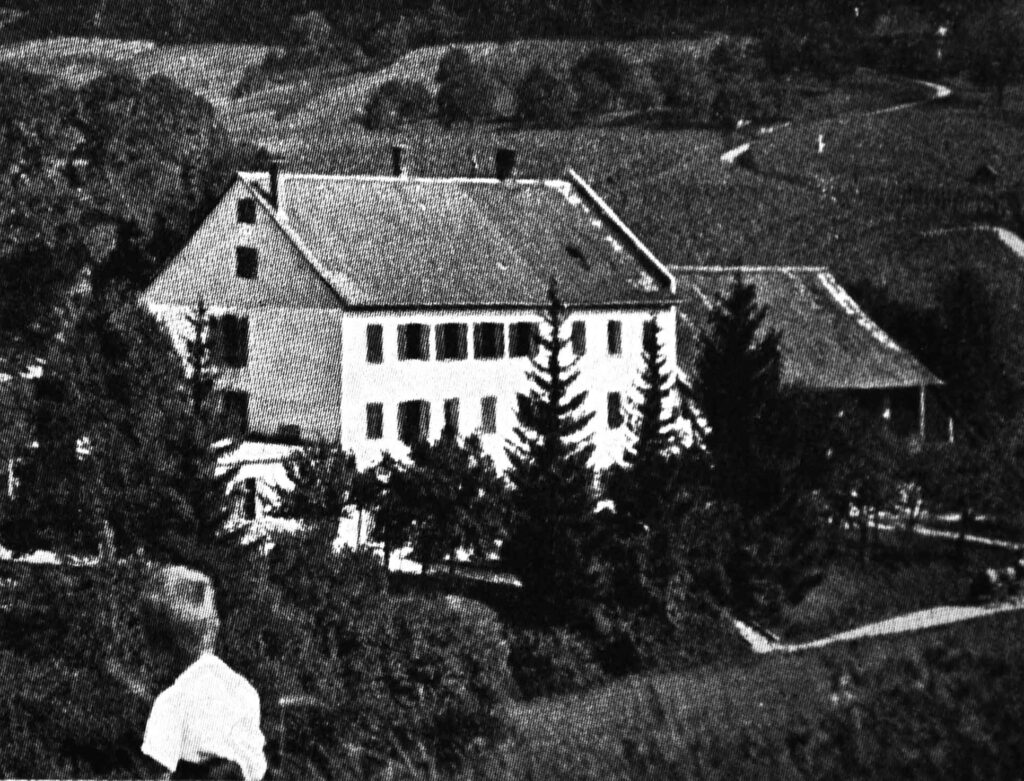 Die Erziehungsanstalt Rorbas in Freienstein von Aussen. Im Vordergrund sieht man den Oberkörper eines Jungen, der in Richtung Erziehungsanstalt schaut. Hinter dem Gebäude ziehen sich Felder.