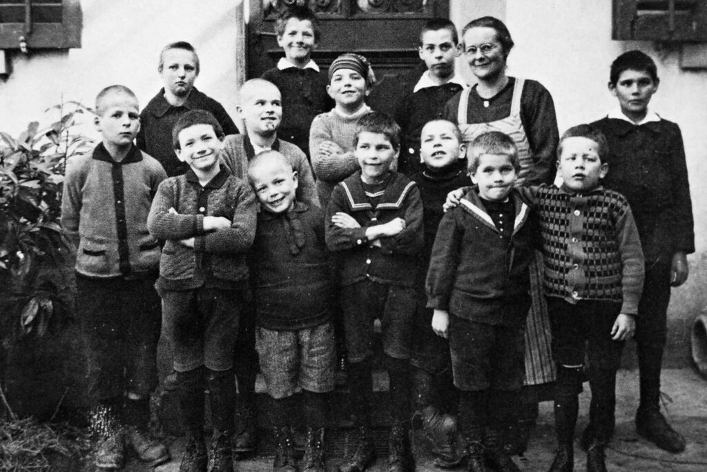 Eine Schulklasse bestehend aus 13 Jungs posieren zusammen mit einer Angestellten vor dem Kinderheim Bühl in Wädenswil.